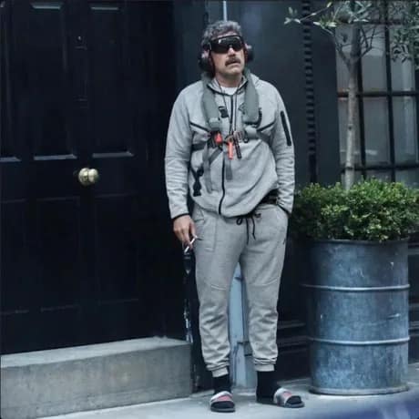 A photo of Nicolas Maduro standing outside wearing a grey tracksuit, sunglasses, and large ear protectors.