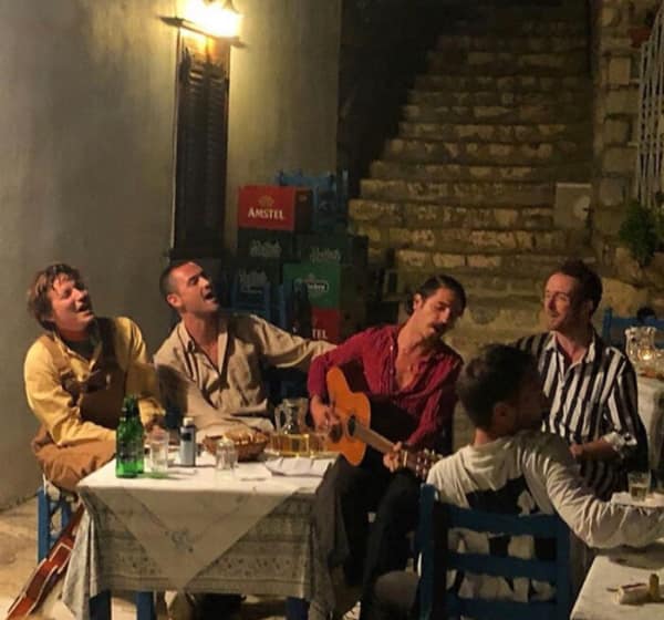 Men singing at an outdoor table at night resembling a tavern painting.