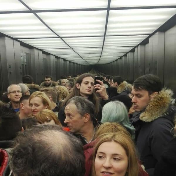 Crowd of people reflected infinitely in a mirrored tunnel or elevator.