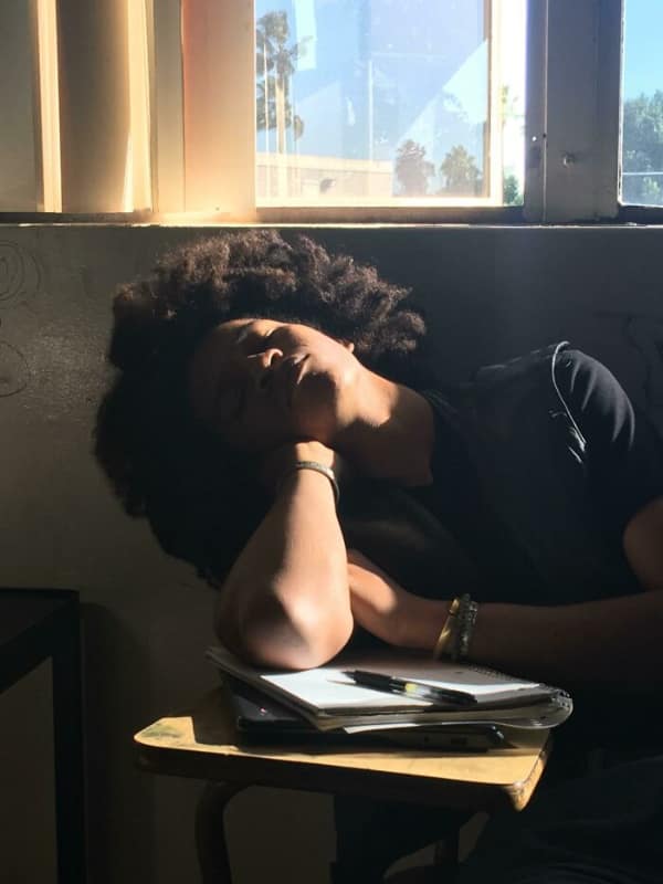 Student sleeping at a desk bathed in a single dramatic shaft of sunlight.