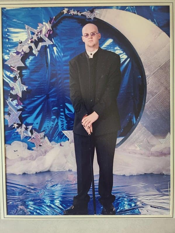 Bald teenager in black suit holding cane at prom blunder years.