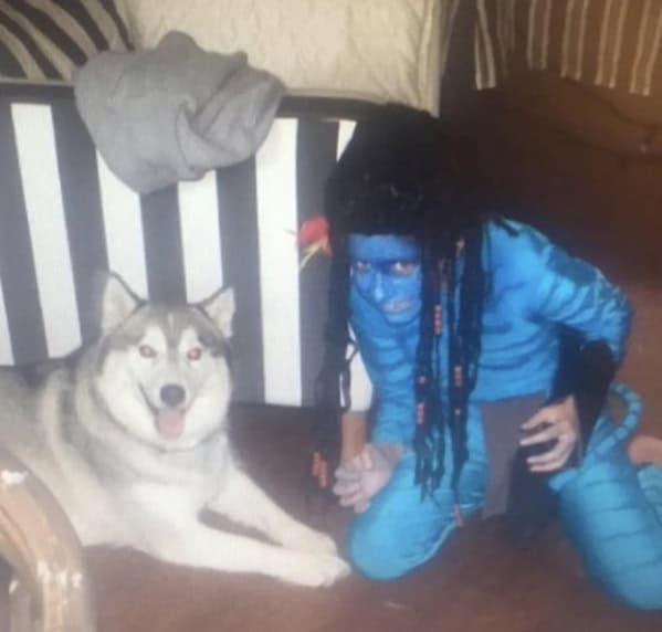 Person in full Avatar blue body paint next to dog blunder years.