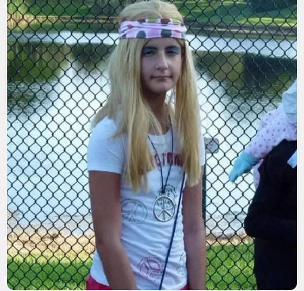 Girl wearing bad blonde wig and peace sign necklace blunder years.