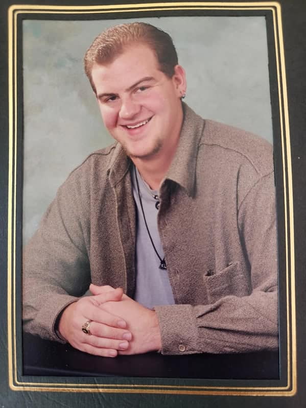 Guy in brown shirt clasping hands for senior portrait blunder years.