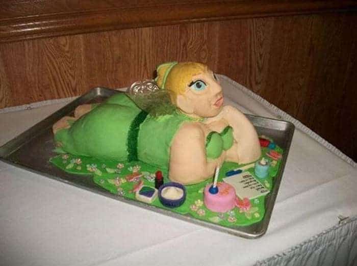 A botched cake of a very large Tinkerbell figure lying on a green base looking distorted.