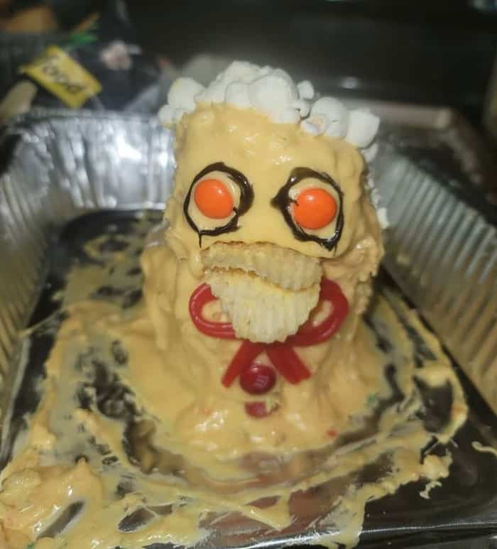 A botched cake that looks like a melting yellow monster with red licorice lips and potato chips for a mouth.