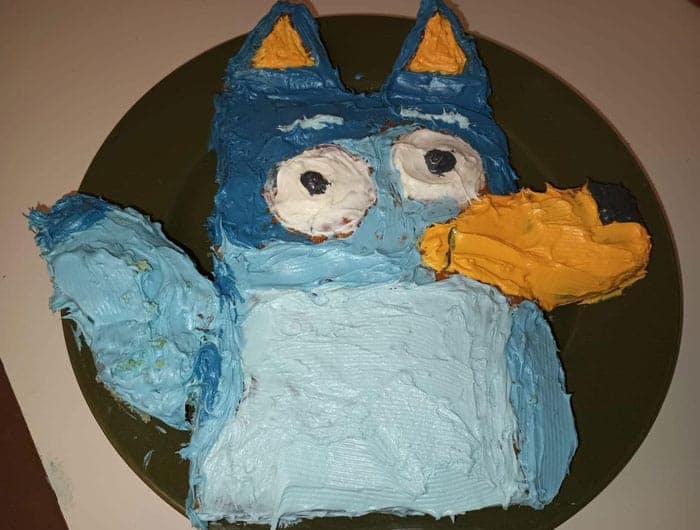 A cake fail of the character Bluey with messy blue icing and a distorted face on a green plate.