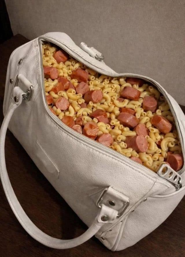 A classic meme photo of a white designer handbag completely filled to the brim with cooked macaroni and sliced hot dogs.