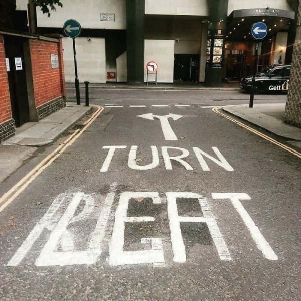 A confusing street sign painted on the road saying Turn Left but with an arrow pointing right.