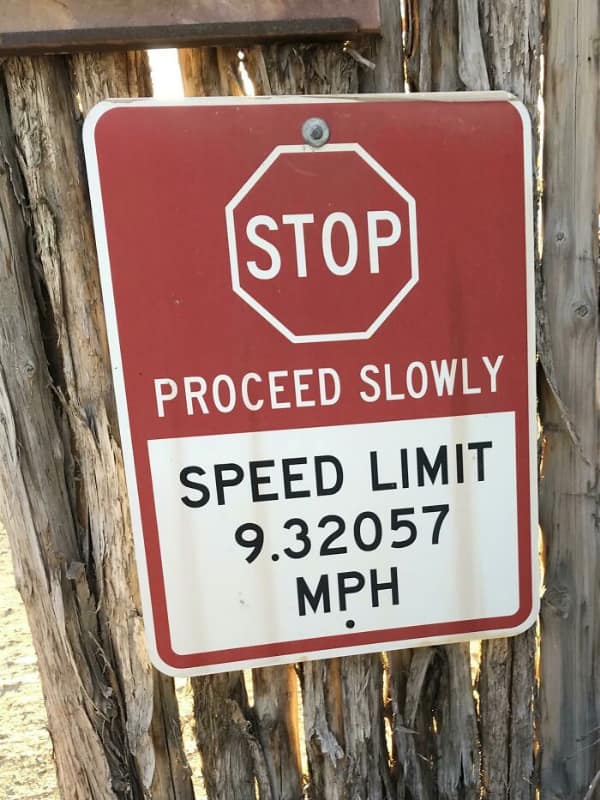 A confusing sign on a fence listing a very specific speed limit of 9.32057 MPH.