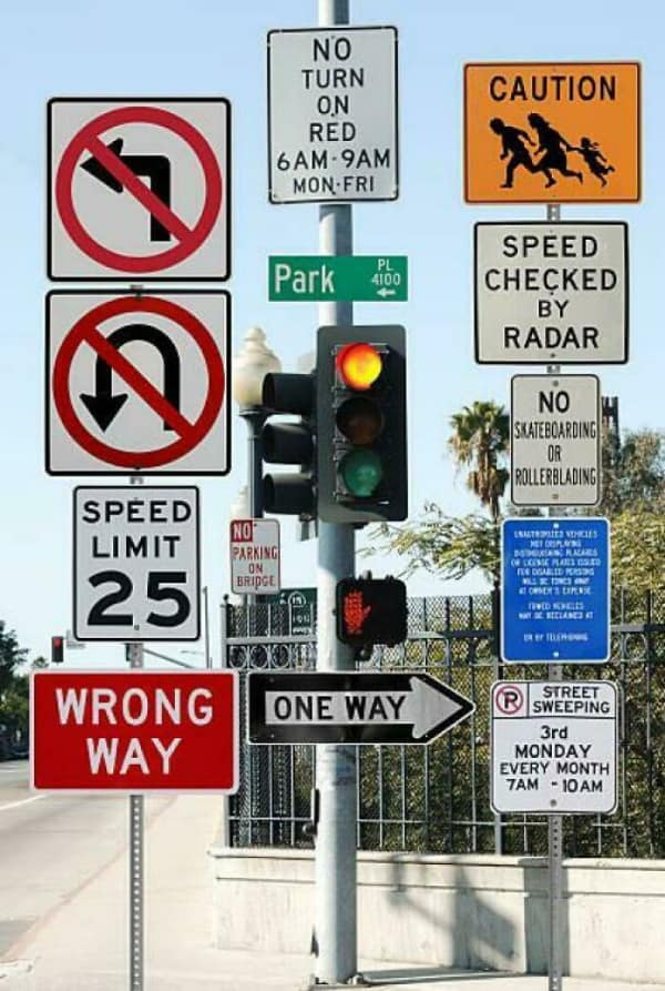 A pole crowded with many confusing street signs including Wrong Way, One Way, and No Turn.