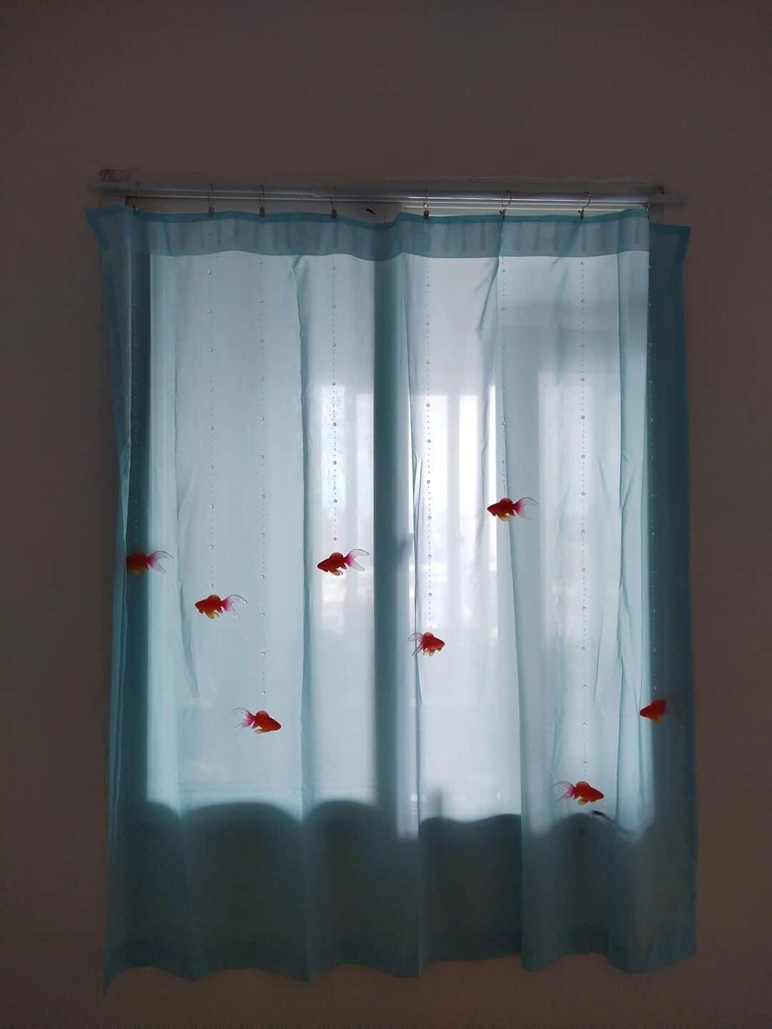 A cool interior design feature showing blue curtains with fake goldfish hanging on strings to look like an aquarium.