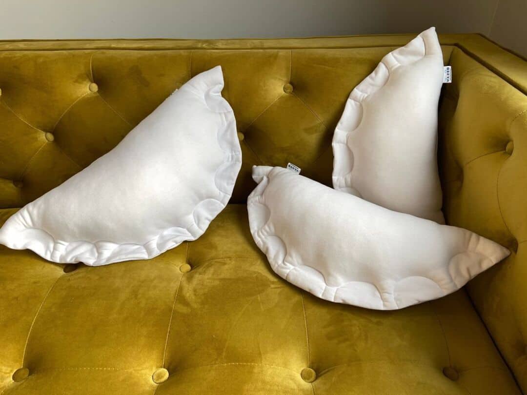 Three white pillows shaped like large dumplings or pierogies on a yellow couch representing awesome interior design