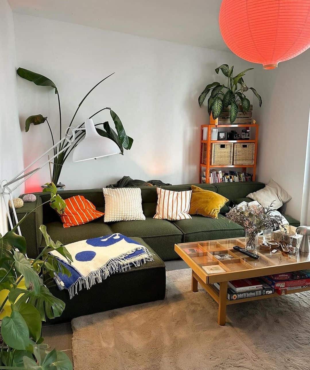 A cool interior design living room with a green sectional sofa, orange paper lantern, and glass coffee table.