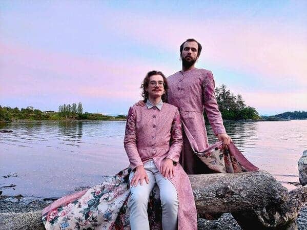 Two men wearing matching pink floral coats sitting by water cottagecore fashion