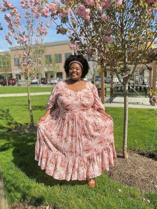 Woman wearing pink floral maxi dress standing under blooming cherry trees cottagecore fashion