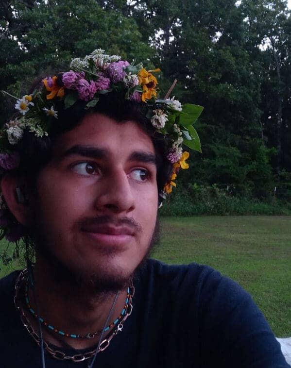 Young man wearing handmade flower crown of clover and wildflowers cottagecore aesthetic