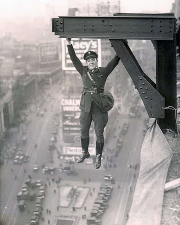 Vintage photo of a man in uniform hanging casually by one hand from a skyscraper beam.