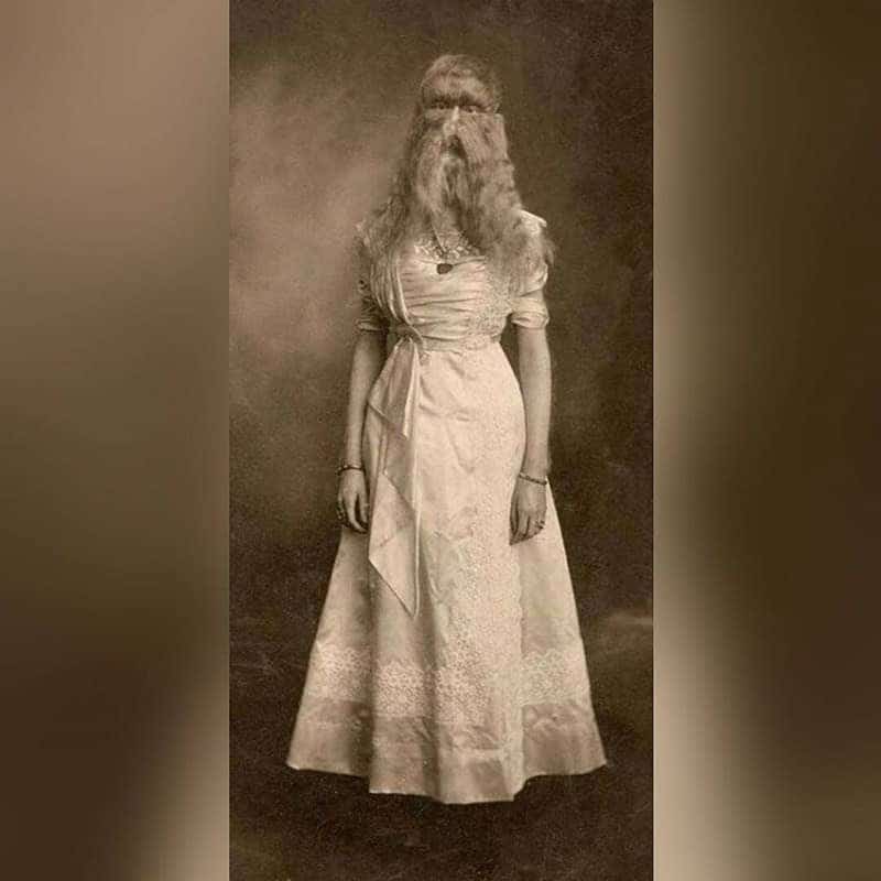 Full body vintage portrait of a woman in a formal dress with a long flowing beard.