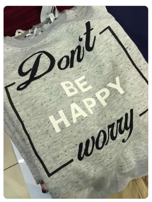 A cursed image of a grey sweatshirt with bad graphic design that reads Don't Be Happy Worry.