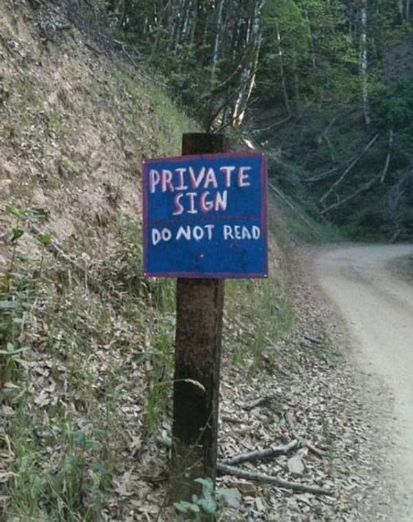 A cursed image of a hand-painted sign in the woods that reads Private Sign Do Not Read.