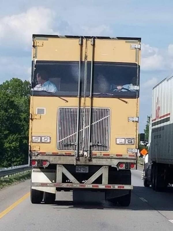 A cursed image of a bizarre, boxy yellow truck driving on a highway that looks like a shed on wheels.