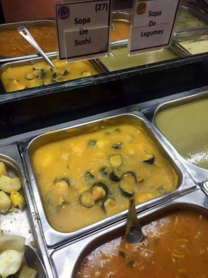 Buffet tray containing yellow soup with whole sushi rolls floating inside.
