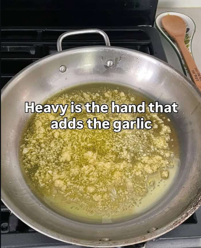 A funny food meme showing a pan with an excessive amount of minced garlic cooking in oil.