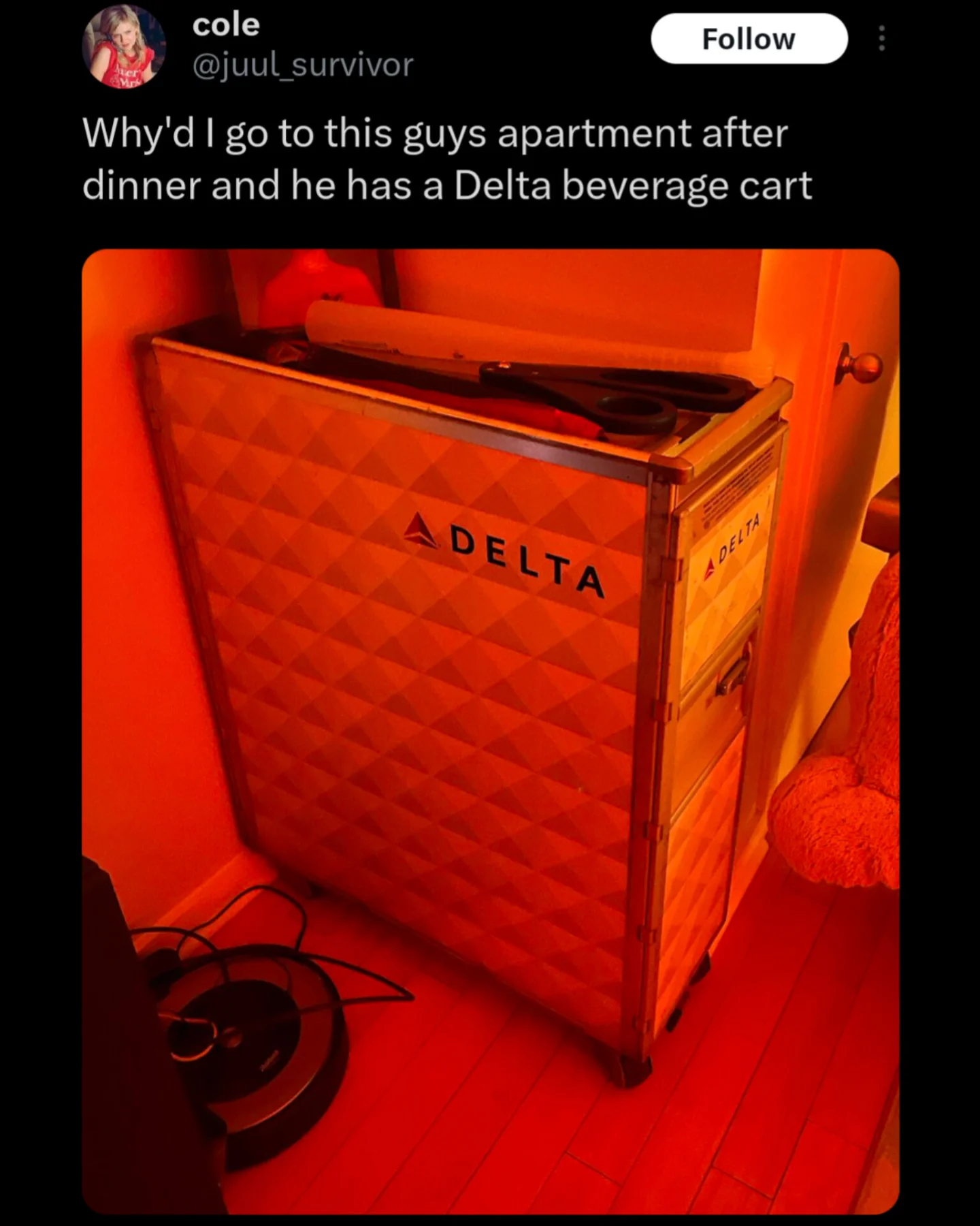 A Delta Airlines beverage cart sitting inside a red-lit residential apartment next to a vacuum.