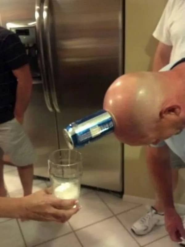 Bald man pouring beer from can stuck to his forehead into glass.