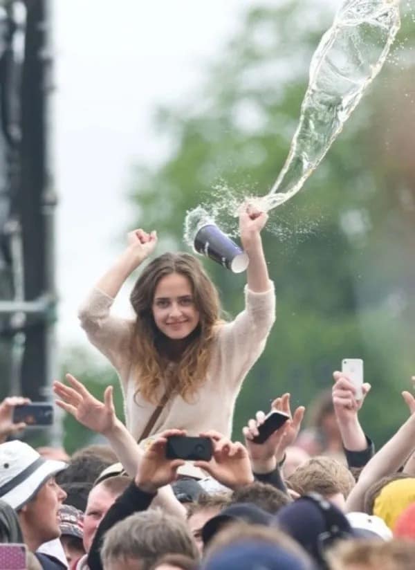 Girl on shoulders at concert throwing drink with liquid suspended in mid-air.