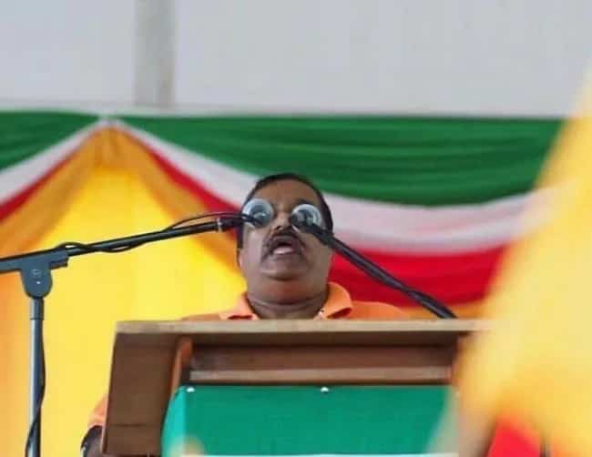 Man at a podium with microphones perfectly aligning with his eyes.