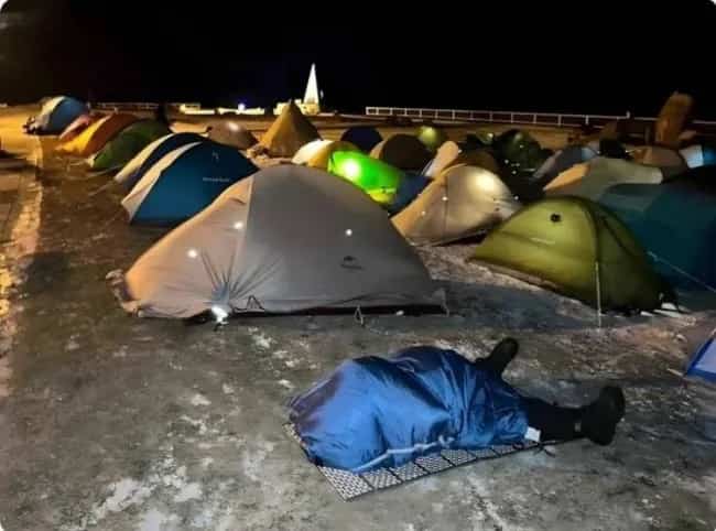 Person sleeping on the ground outside while everyone else is in tents.
