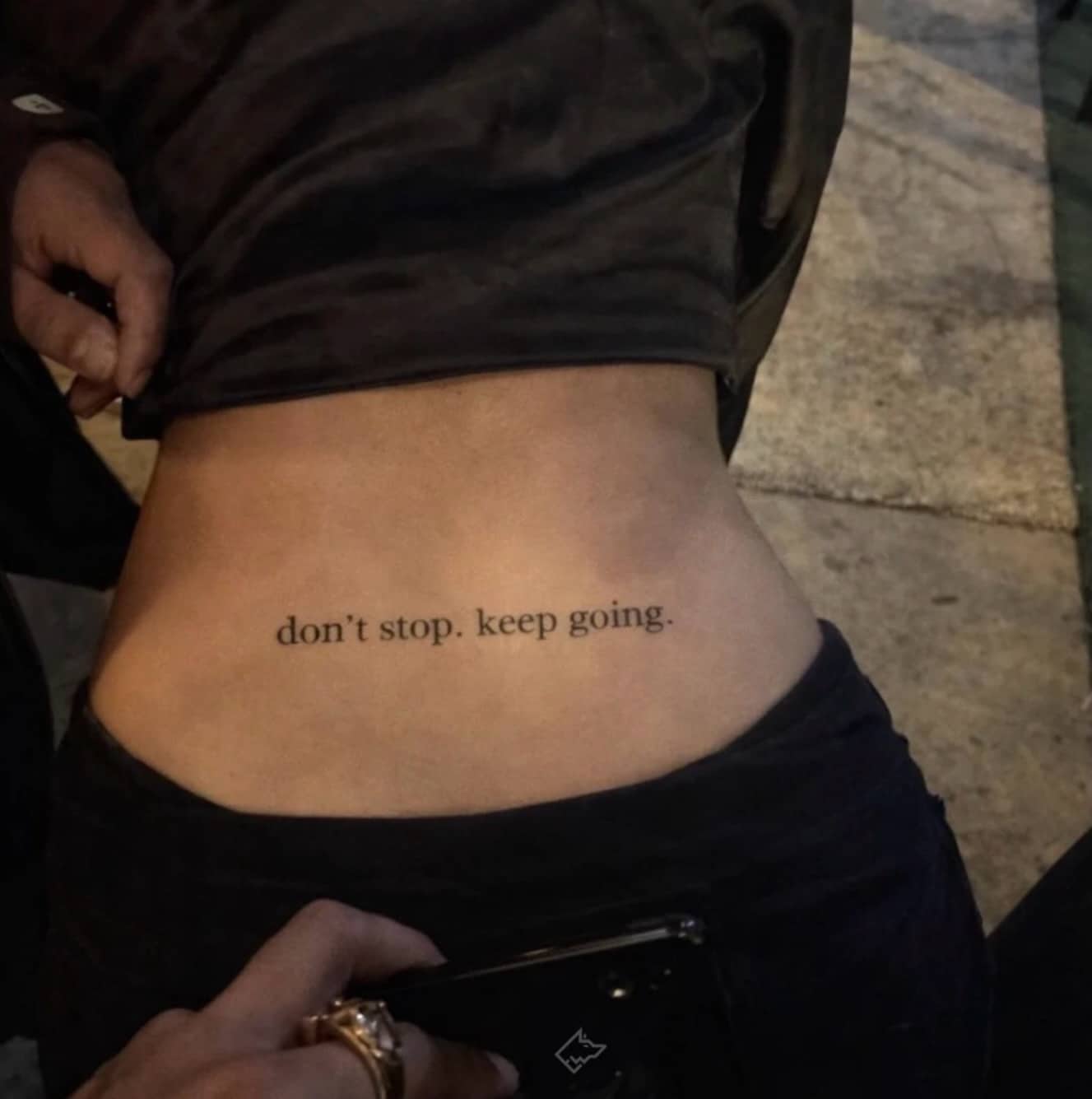 Lower back tattoo on a woman reading "don't stop keep going" viewed from behind.