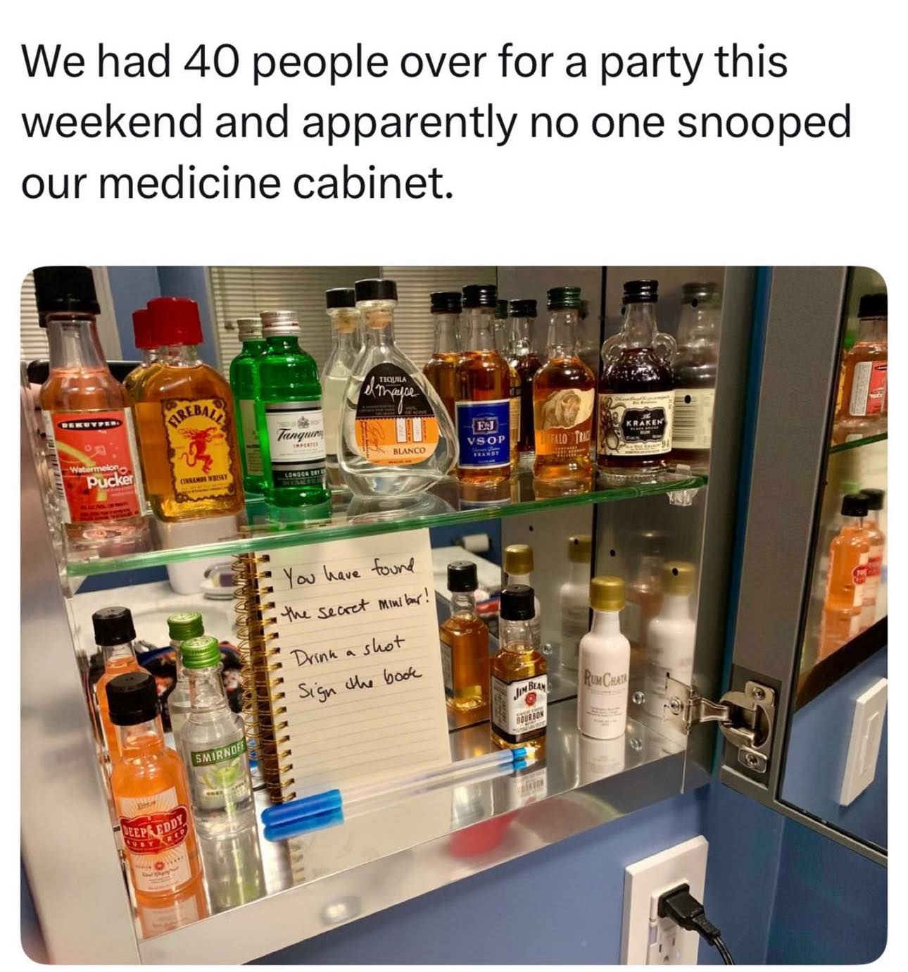 Open bathroom medicine cabinet revealing a secret mini bar hidden behind the mirror with liquor bottles.