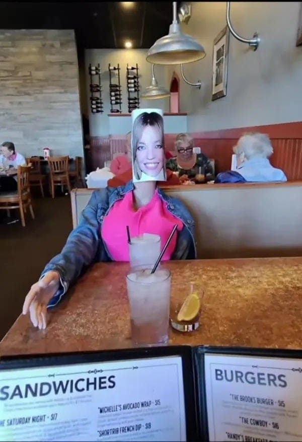 Diner sitting at a restaurant table with a menu featuring a woman's face placed over their own head.