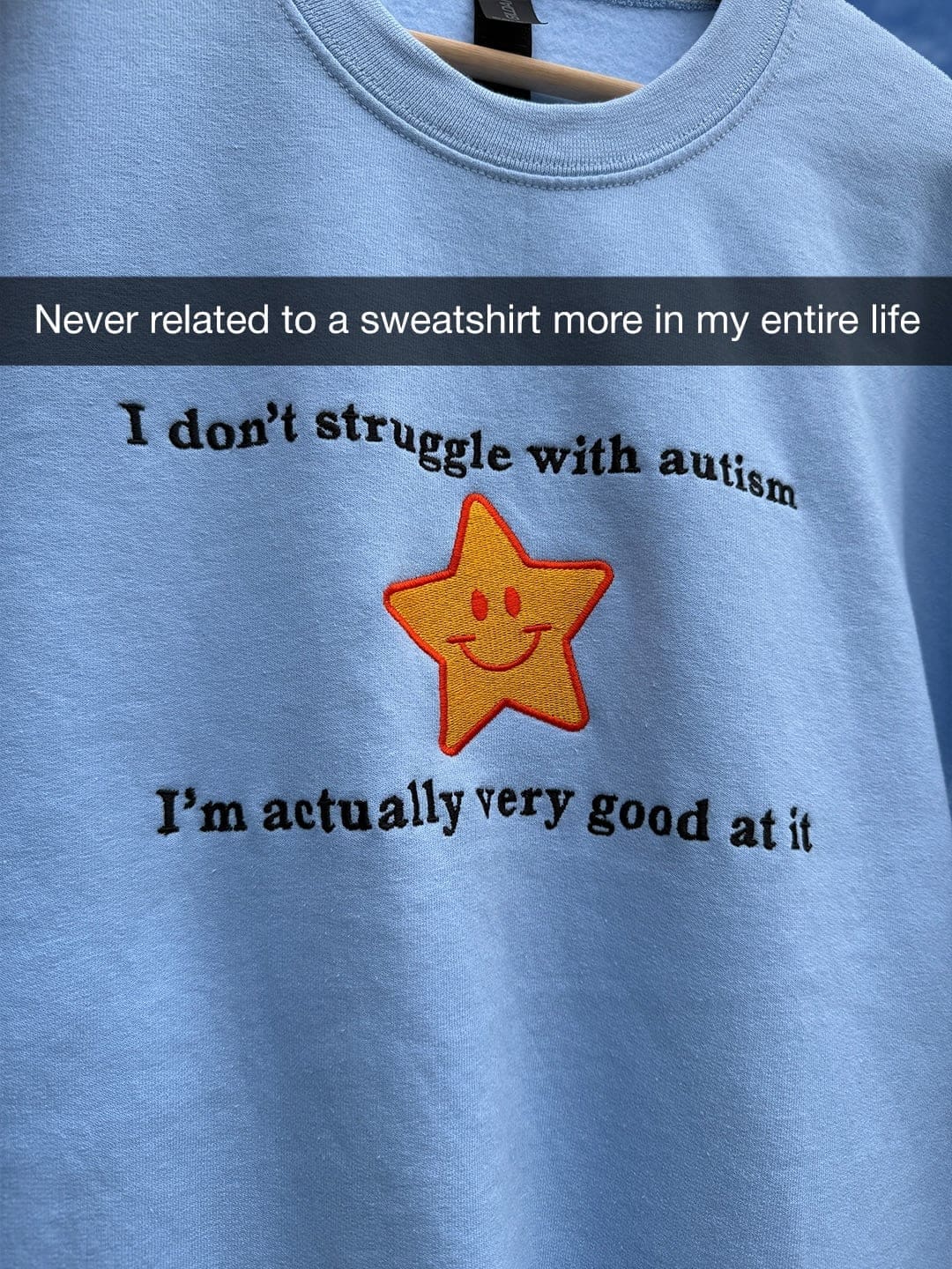 Blue sweatshirt embroidered with a gold star and a joke about being "very good" at autism instead of struggling.