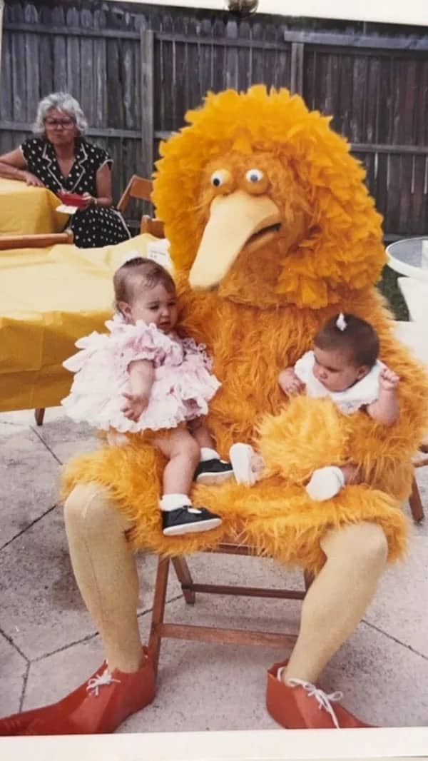 Vintage photo of terrifying Big Bird mascot holding two babies on lap.