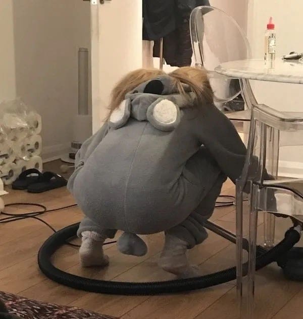 Child wearing a gray koala onesie squatting in a strange pose on the floor.