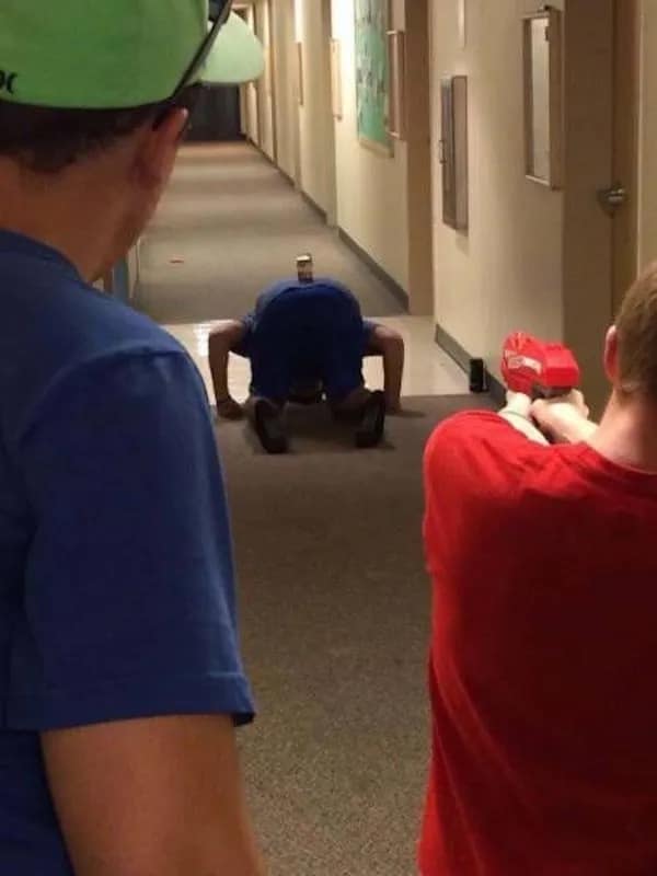 Person on floor with can on butt being held at gunpoint by nerf gun funny pic.