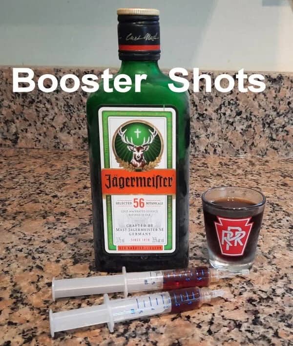 Bottle of Jagermeister liqueur next to two medical syringes filled with liquid.