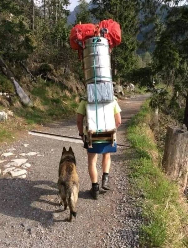 Hiker walking a trail with a large metal beer keg strapped to his backpack.