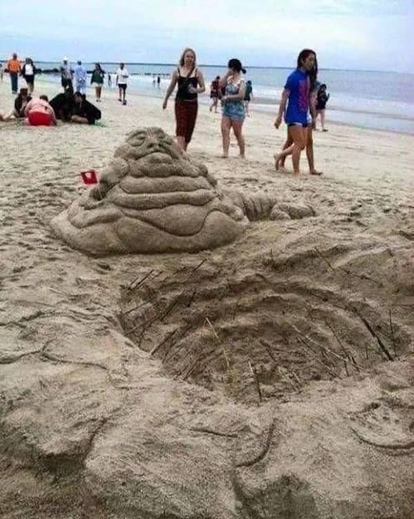 Sand sculpture of Jabba the Hutt next to a Sarlacc pit hole on a beach.