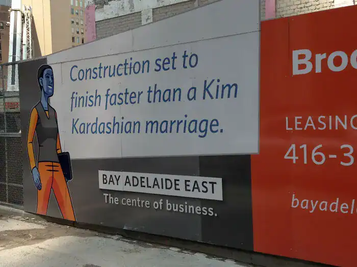 A funny print ad on a construction barrier claiming the building will finish faster than a "Kim Kardashian marriage."