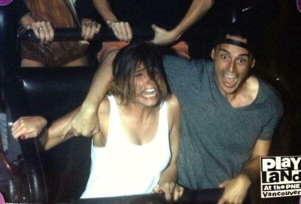 A funny rollercoaster picture of a woman screaming in terror while a man cheers and a hand reaches out from behind