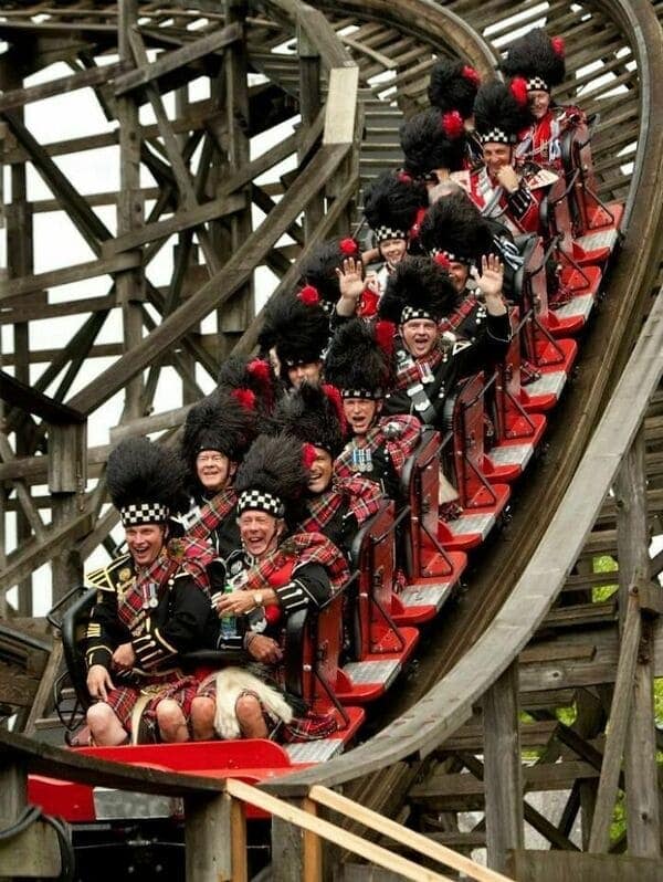 A funny rollercoaster picture of a full Scottish pipe band playing bagpipes while riding a wooden rollercoaster.