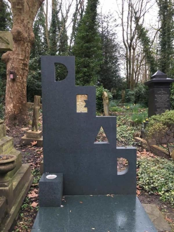 A modern funny tombstone sculpture spelling out the word DEAD in large stacked letters.
