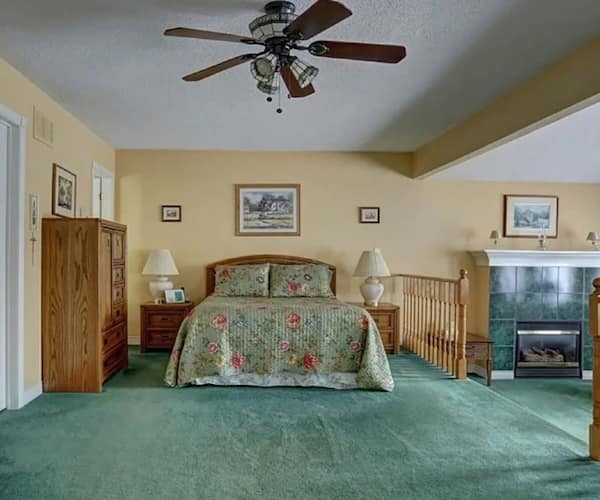Bedroom with green carpet, wooden furniture, and floral green and maroon bedding.