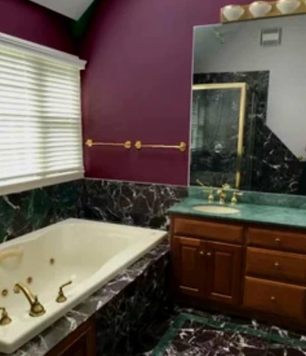 Bathroom with maroon walls, green marble vanity, and gold bathtub fixtures.