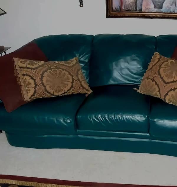 Teal green leather sofa styled with maroon and paisley decorative pillows.